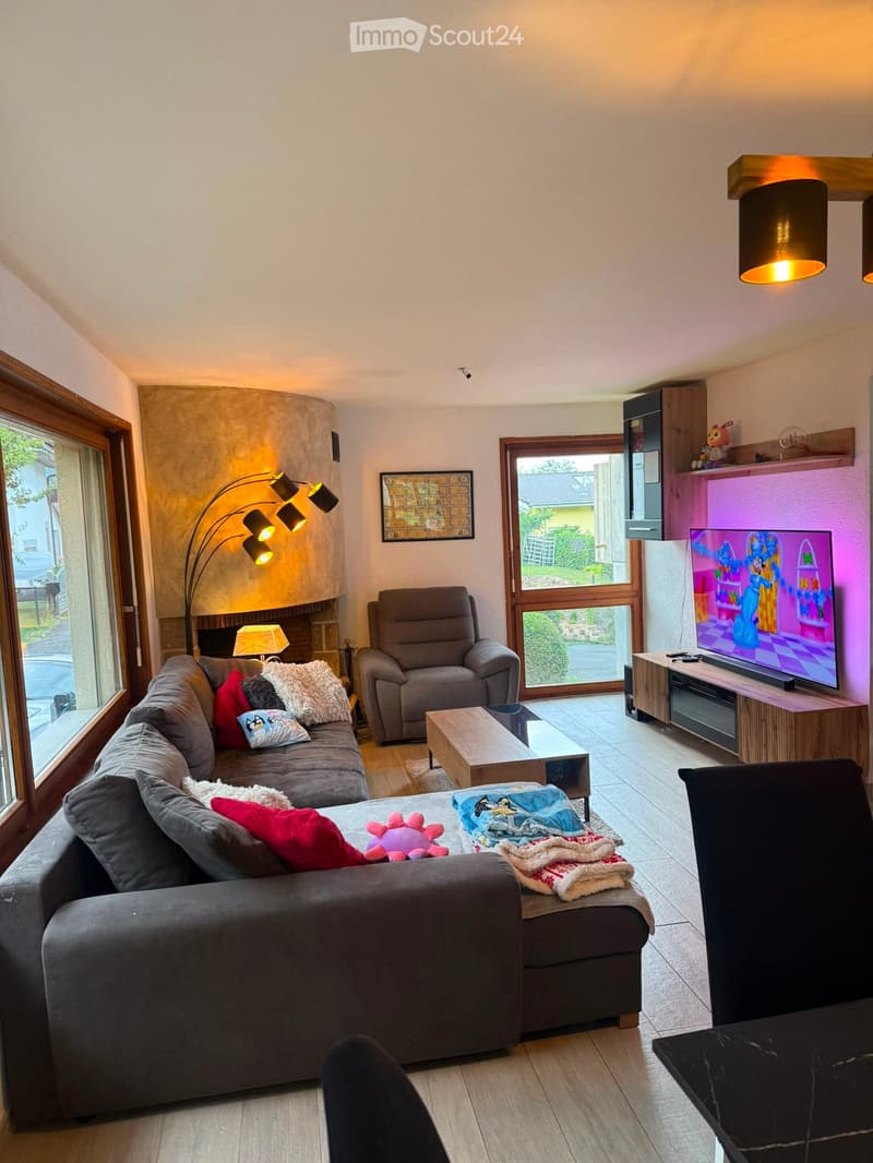 Modern living room with large windows, grey sectional sofa, armchair, coffee table, TV, and decorative lighting.