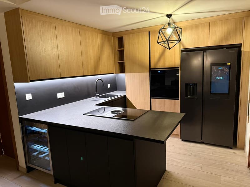 Modern kitchen with wooden cabinets, stainless steel appliances, island with sink and induction cooktop, and pendant lighting.