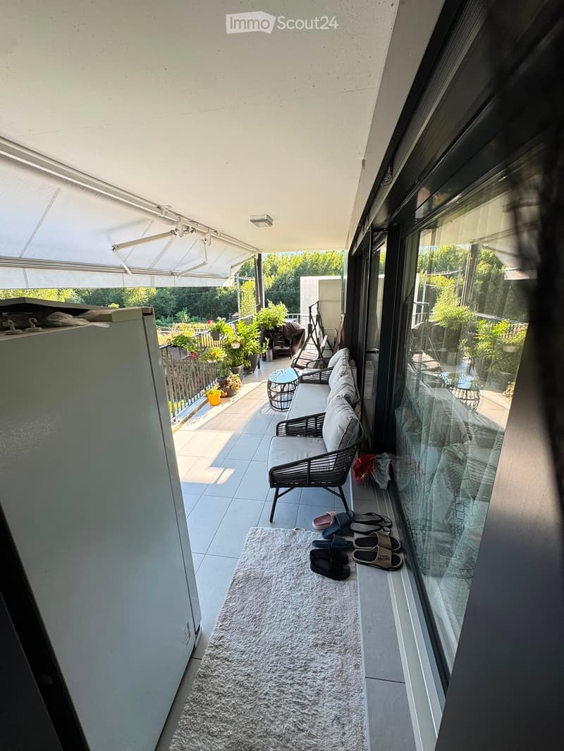 Balcony with a sofa, small table, chairs, a white rug, and several pairs of sandals placed near the glass door.