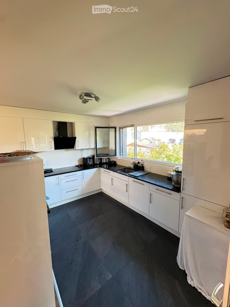 Modern kitchen with white cabinets, black countertops, and dark tiled flooring. Features a sink, faucet, blender, toaster, microwave, and refrigerator.