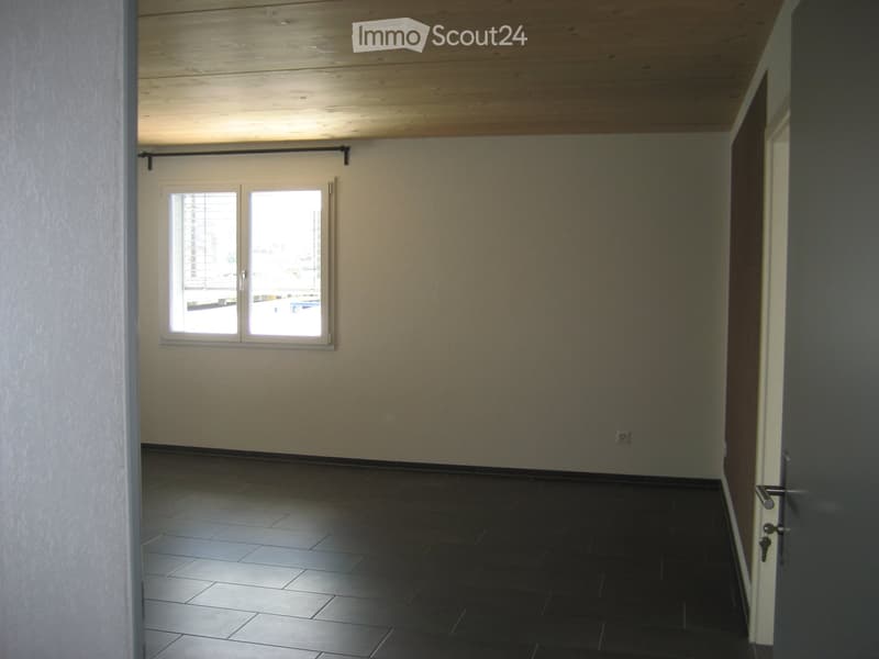 Empty room with dark tiled floor, light-colored walls, and a large window with blinds. Wooden ceiling and a door visible on the right side.