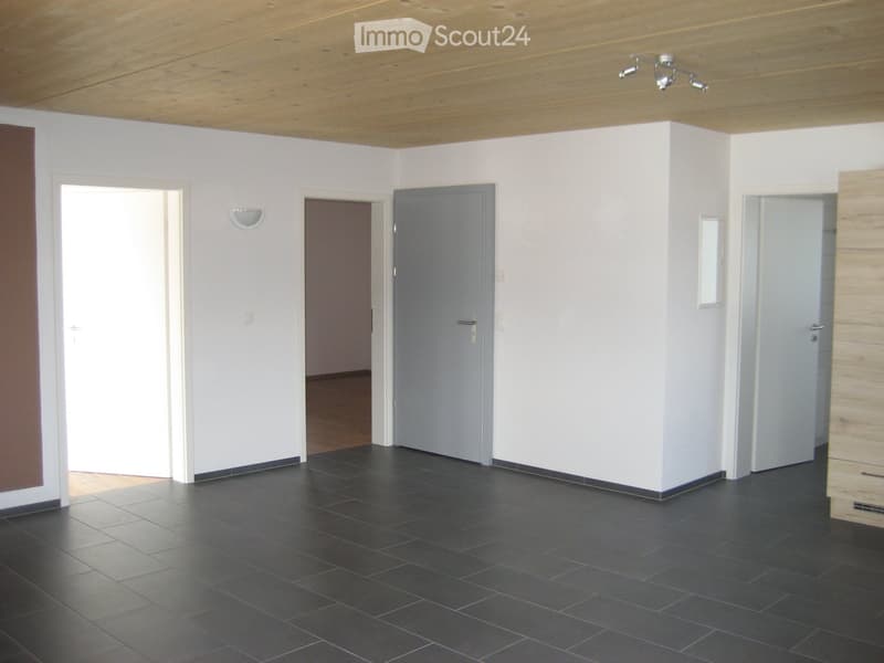 Empty room with white walls, dark tiled floor, wooden ceiling, and several doors leading to other spaces.