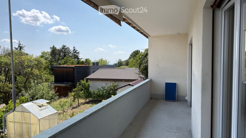 Balcony with a view of a garden and neighboring houses, featuring a railing and a blue board leaning against the wall.