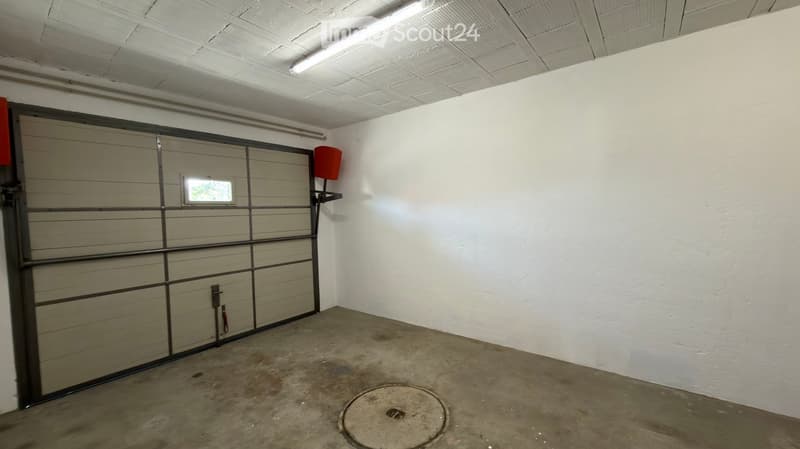Empty garage with a large, closed garage door, white walls, and a concrete floor.