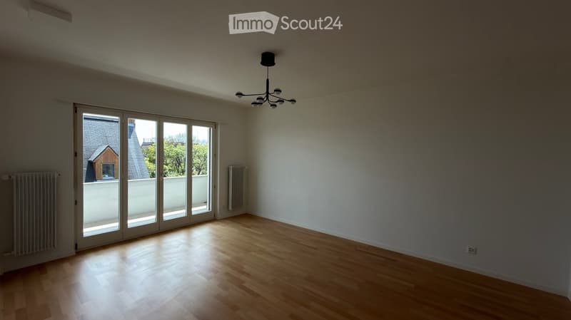 Empty room with wooden flooring, white walls, large sliding glass doors, and a chandelier light fixture.