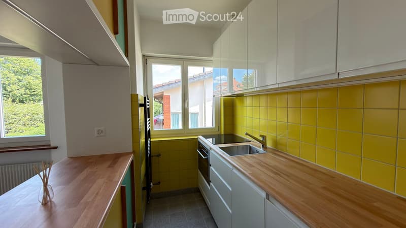 Modern kitchen with light wooden countertops, white cabinets, and yellow tiled backsplash. Features a sink, faucet, and built-in oven.