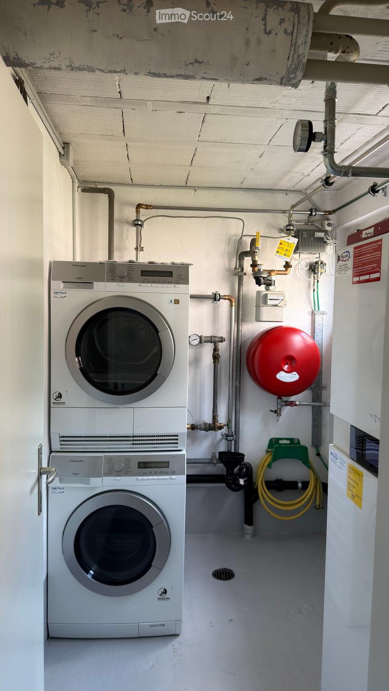 Utility room with a stacked washing machine and dryer, water heater, pipes, valves, and a pressure vessel.