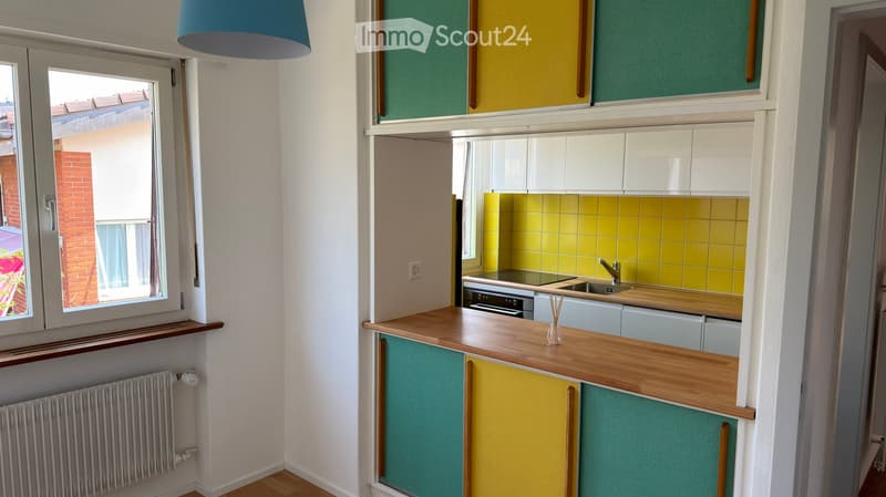 Modern kitchen with colorful cabinets, wooden countertop, sink, and oven. Features a window with a view of a brick building and a radiator below.
