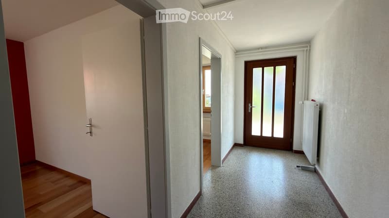 Empty hallway with light-colored walls, carpeted floor, and wooden doors at both ends.
