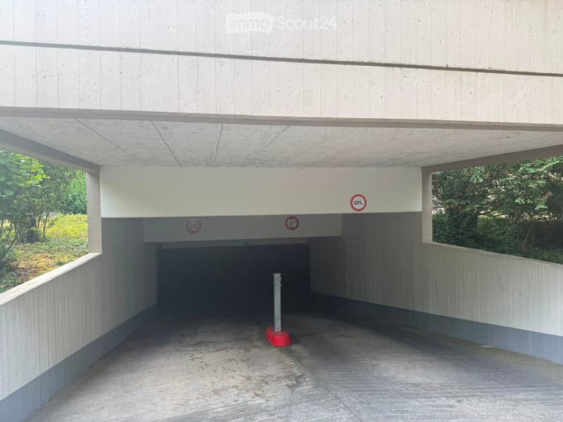 Modern concrete structure with a covered entrance, featuring a raised ground floor and visible signage indicating parking details.