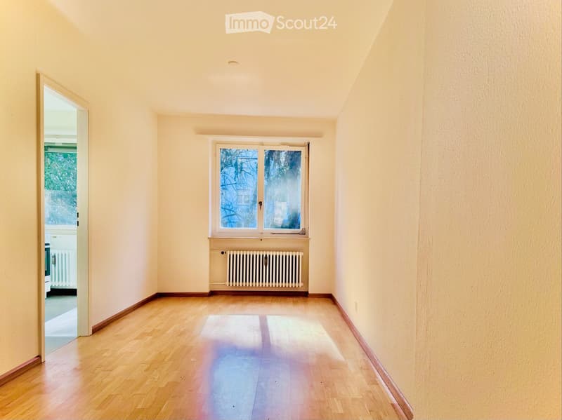 Empty room with wooden flooring, light-colored walls, a window with a radiator below, and an open doorway leading to another space.
