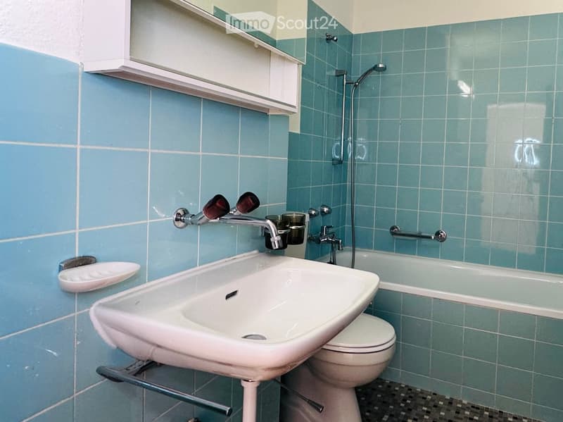 Bathroom with blue tiled walls, white sink, toilet, bathtub, and showerhead. Includes a cabinet above the sink and a towel rack.