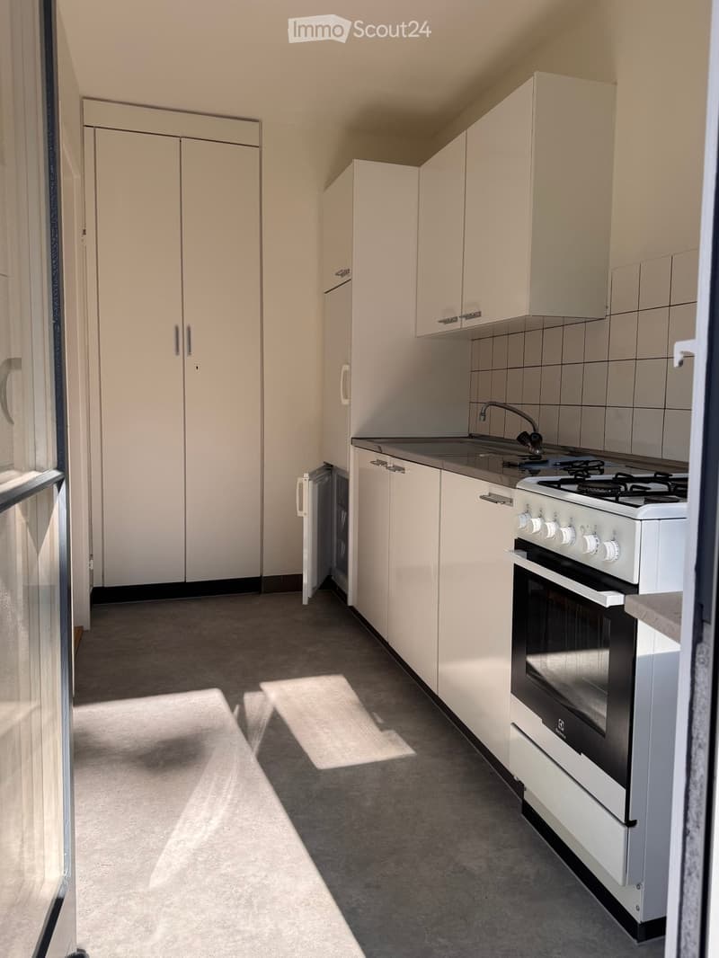 Modern kitchen with white cabinets, a sink, a gas stove, and an oven. The space is well-lit with natural light coming through a window on the left.