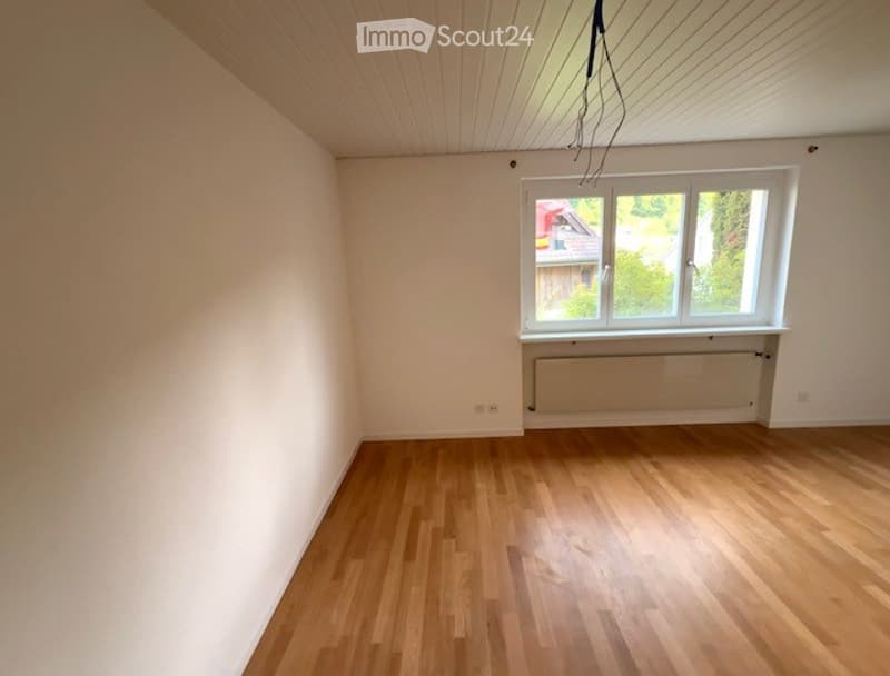 Empty room with wooden flooring, white walls, and a single window with a radiator below it.