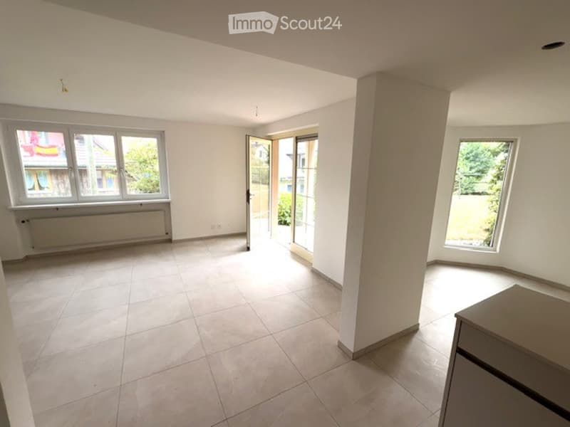 Empty room with tiled floor, white walls, large windows, and a sliding glass door leading to an outdoor area.