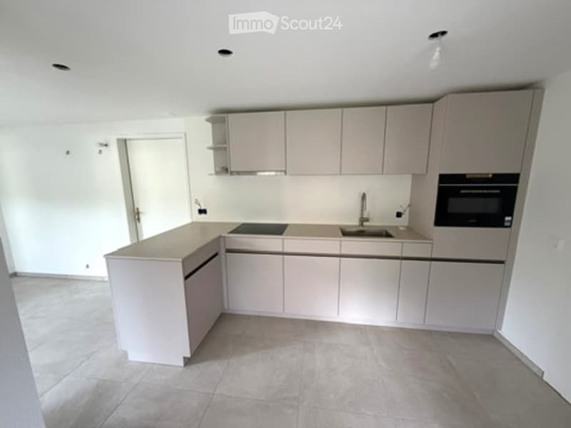Modern, minimalist kitchen with light grey cabinets, a central island, and built-in appliances including a sink, faucet, and oven. The space features a clean, uncluttered design with neutral tones and ample lighting.