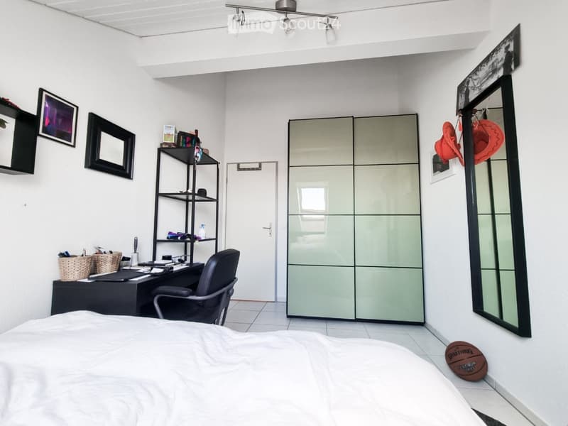 Modern bedroom with a bed, desk, chair, mirror, and shelves. Features a large closet with mirrored doors and decorative items on the walls.