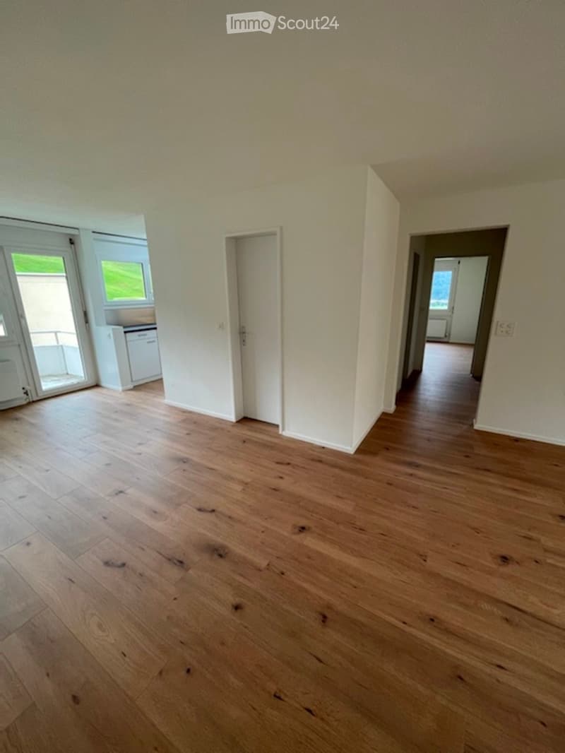Empty hallway with wooden flooring and white walls, featuring a staircase leading upwards and a window at the top.