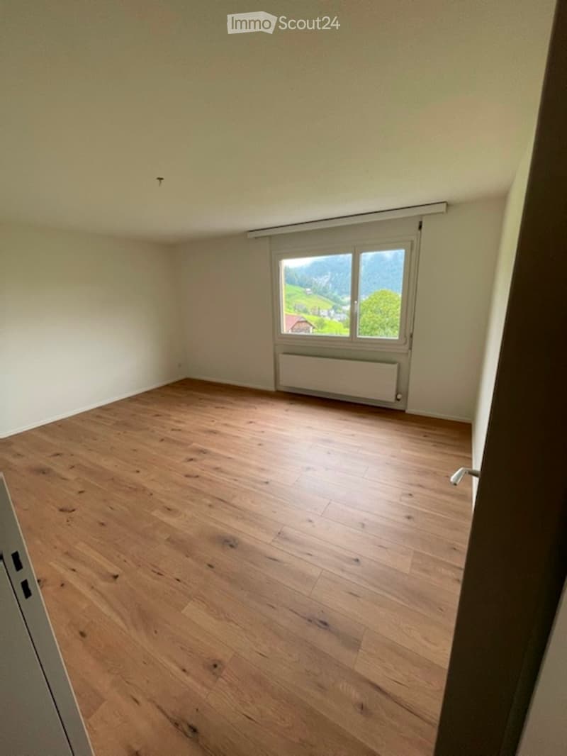 Empty room with wooden flooring, white walls, and a window showing a scenic outdoor view.
