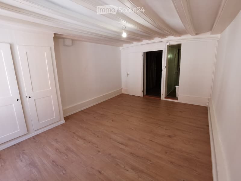 Empty room with white walls, wooden flooring, two white doors, and an open door leading to another room