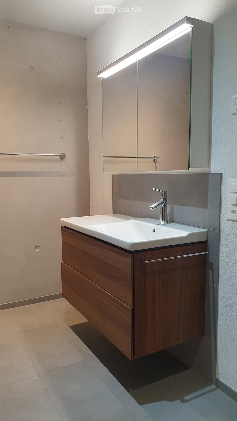 Modern bathroom with a white sink, wooden cabinet, chrome faucet, and illuminated mirror above.