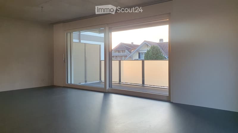 Empty room with large sliding glass doors leading to a balcony, dark flooring, and natural light streaming in.