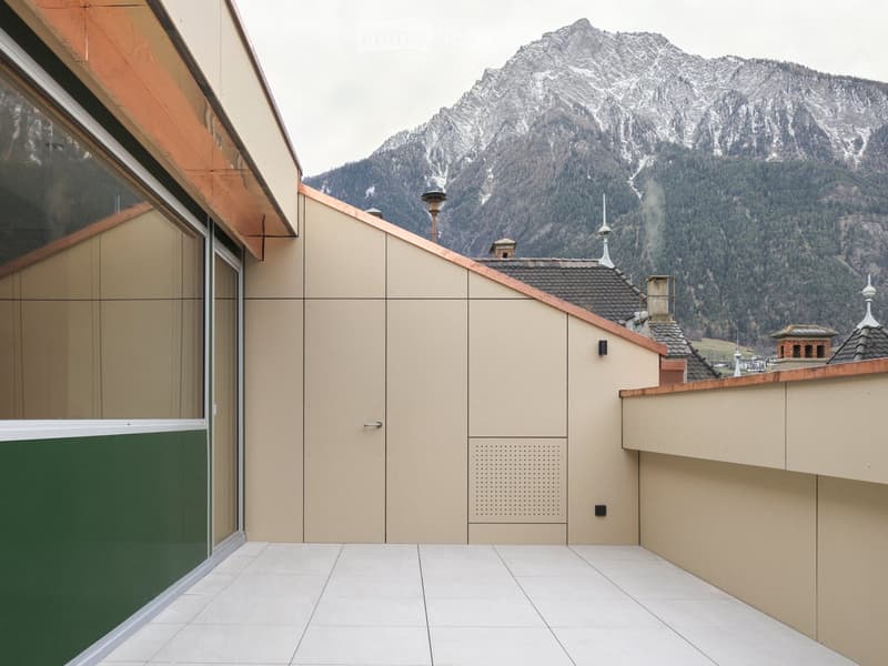 Balcony with white tiled floor, beige walls, and a view of snow-capped mountains.