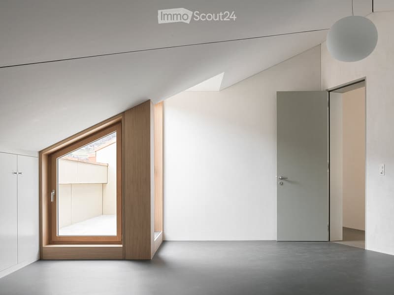 Modern, minimalist unfurnished room with white walls, grey floor, large window with wooden frame, and a hanging spherical light fixture.