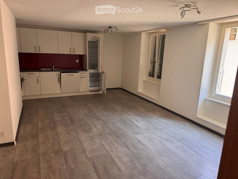 Empty kitchen with light-colored cabinets, a refrigerator, and a sink, featuring tiled flooring and large windows.