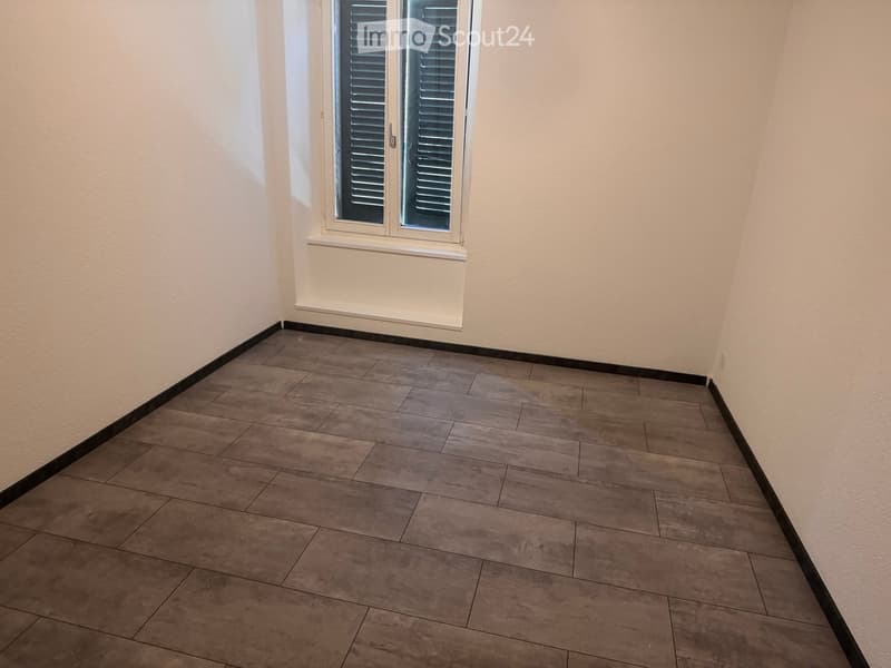Empty room with tiled floor and white walls, featuring a window with shutters.