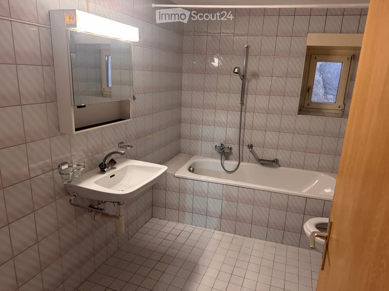 Bathroom with tiled walls and floor, featuring a sink, bathtub, mirror, and toilet. The sink has a modern faucet, and the bathtub includes a handheld showerhead.