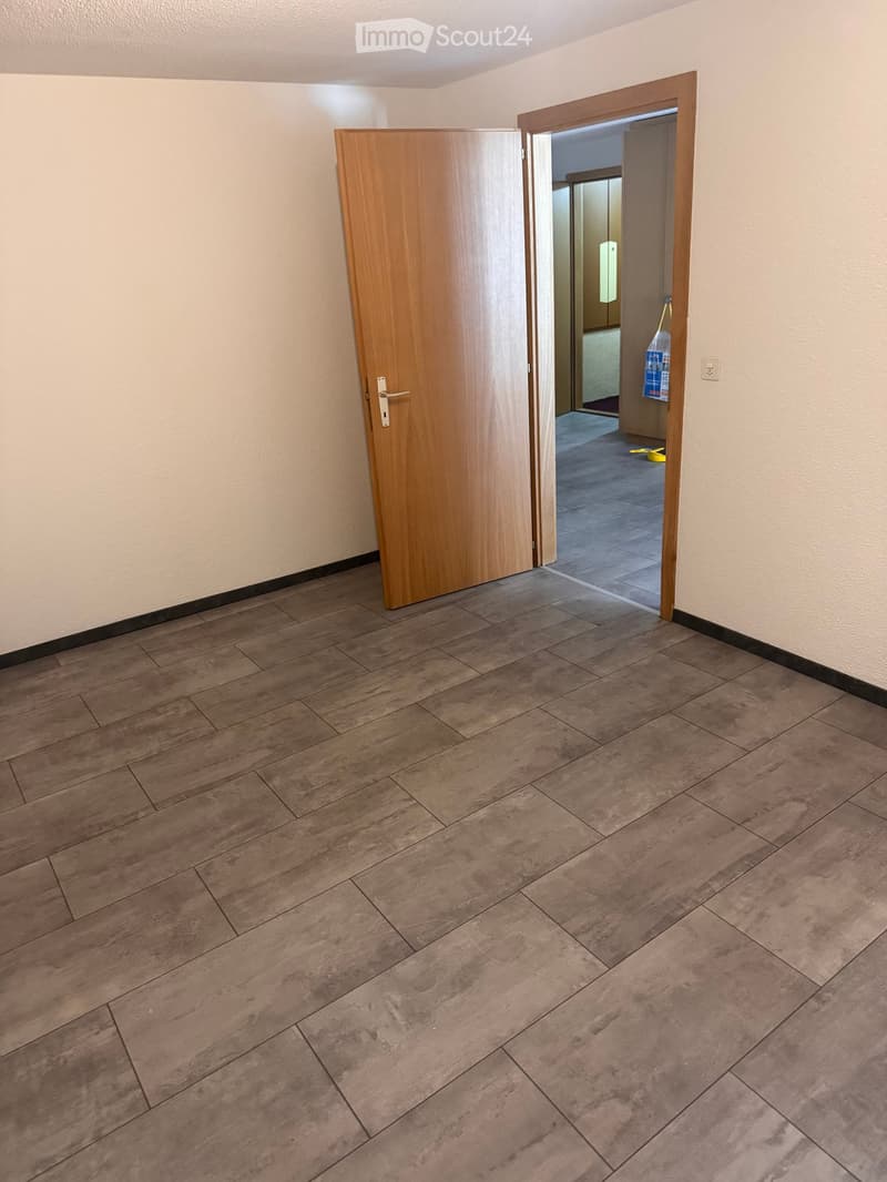 Empty hallway with wooden doors and tiled floor, leading to another room.