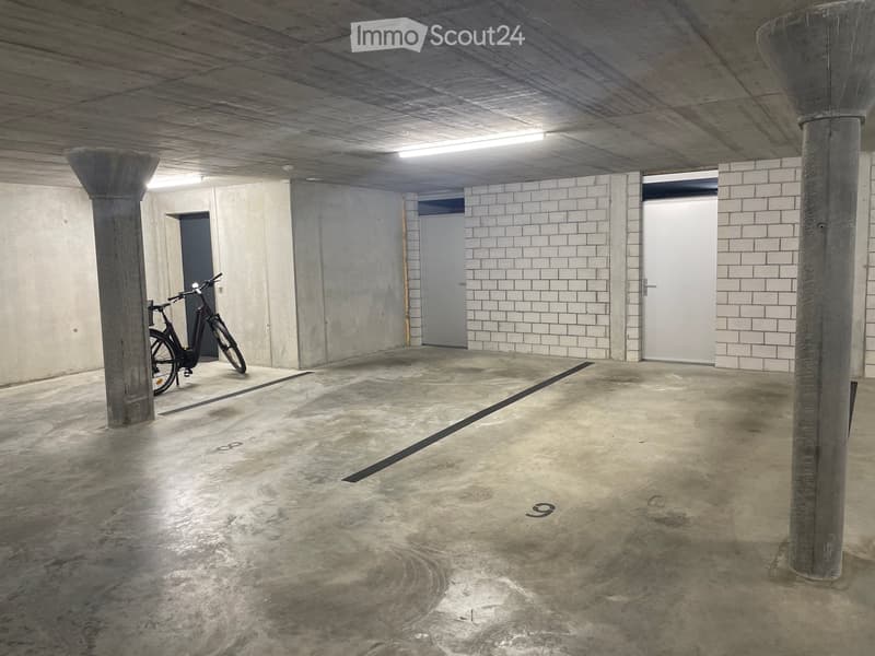 Underground parking area with concrete pillars, tiled walls, and a single bicycle parked against a pillar.