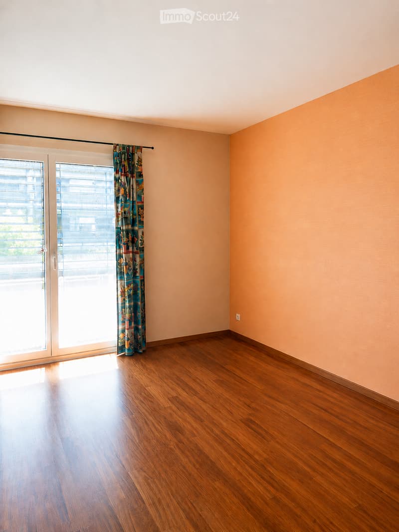 Empty room with wooden flooring, light-colored walls, and a sliding glass door with a curtain partially drawn.
