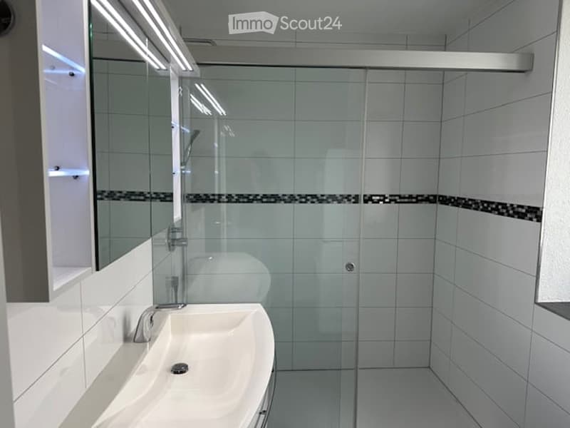 Modern bathroom with white tiles, a glass shower enclosure, a sink with a mirror, and built-in storage.