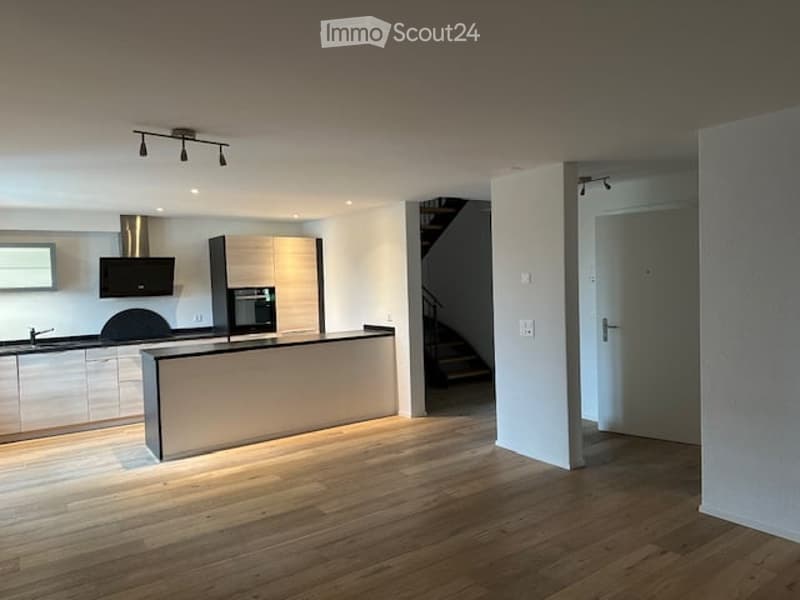 Modern kitchen with light wood flooring, white cabinets, stainless steel appliances, and a central island.