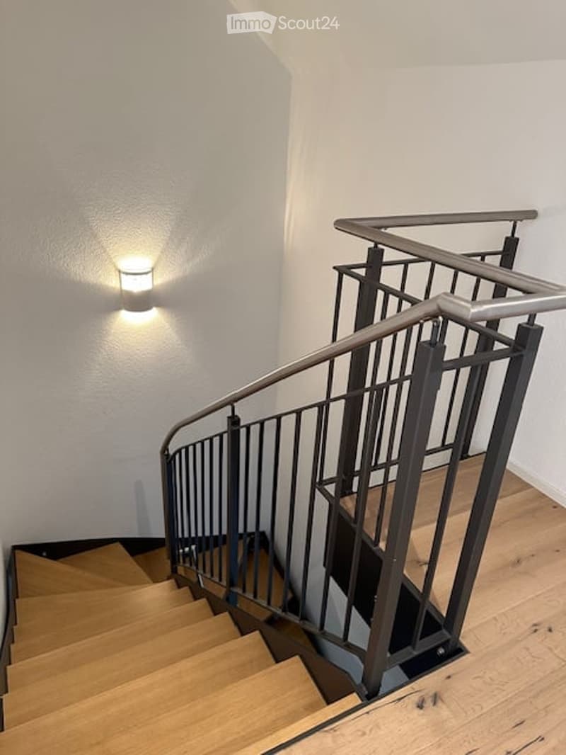 Modern staircase with wooden steps and metal railing, illuminated by a wall-mounted light fixture.