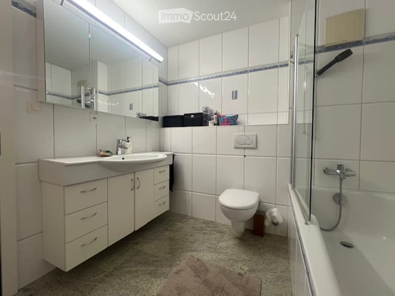Modern bathroom with white tiled walls, a double sink vanity, a toilet, a bathtub, and a towel on the floor.