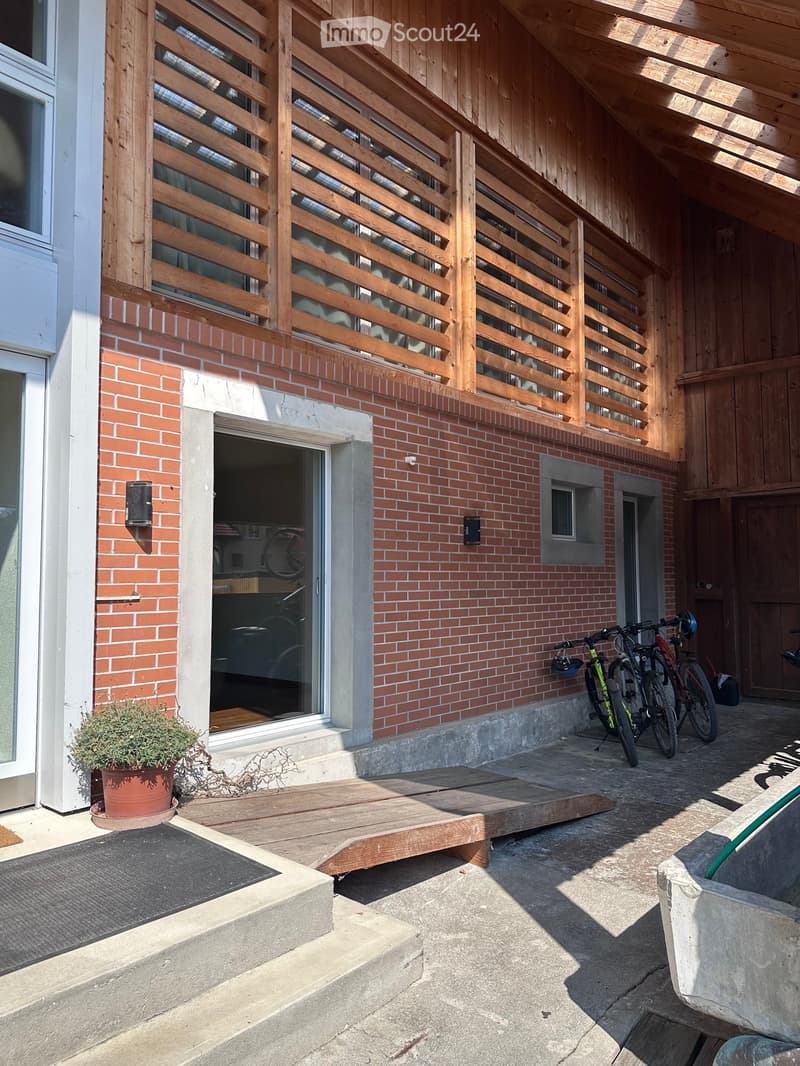 Outdoor area with wooden deck, brick wall, bicycles, potted plant, and raised ground floor.