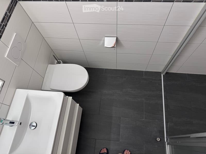 Modern bathroom with white toilet, white sink, and dark grey tiles on the floor and walls.