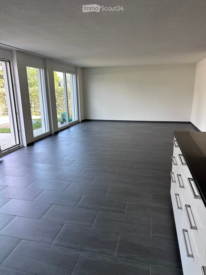 Empty room with grey tiled floor, white walls, large sliding glass doors leading to outdoor area, and a white cabinet with silver handles on the right side.