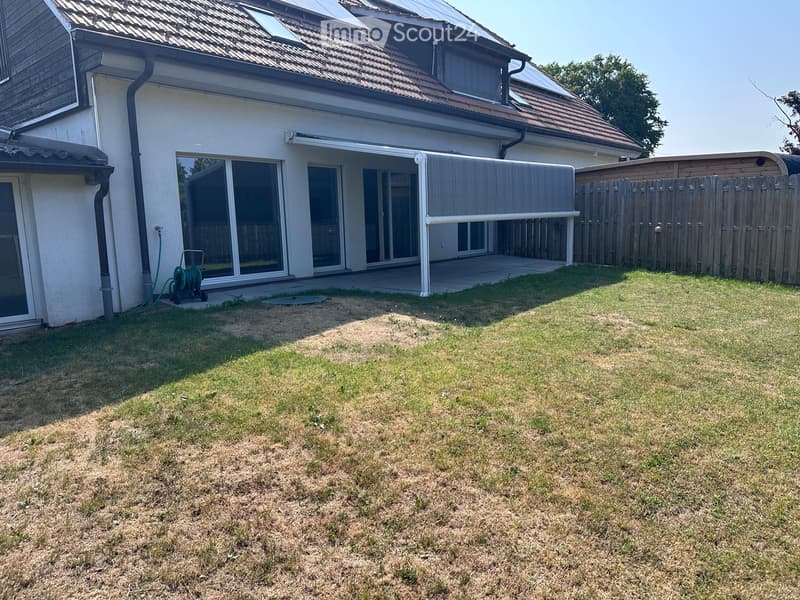 Lawn area in front of a house with a covered patio, wooden fence, and solar panels on the roof.