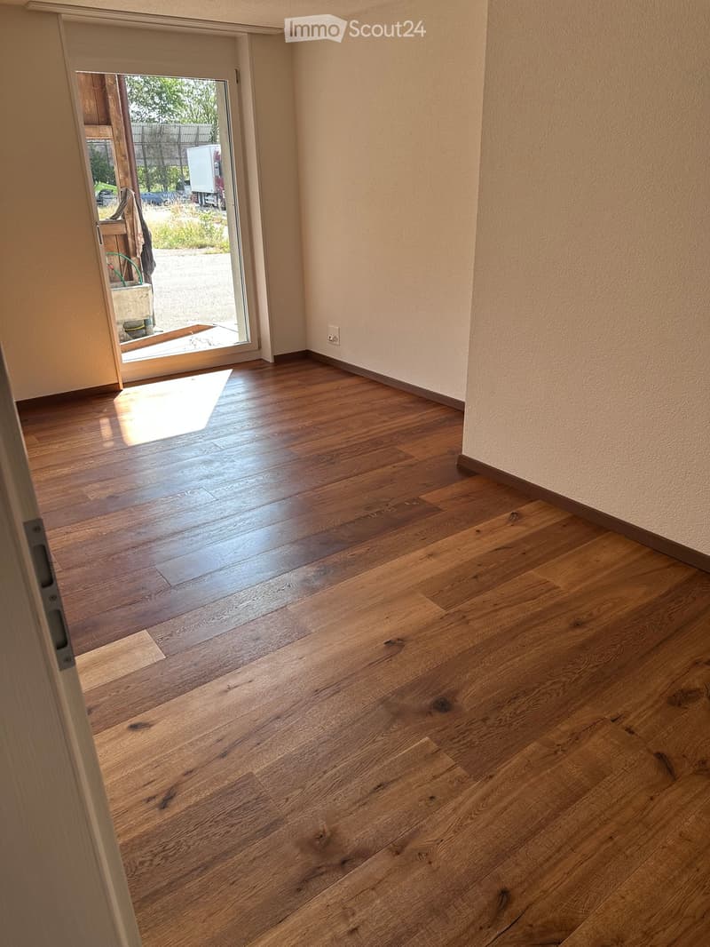 Empty room with wooden flooring and light-colored walls, featuring a sliding glass door leading outside.