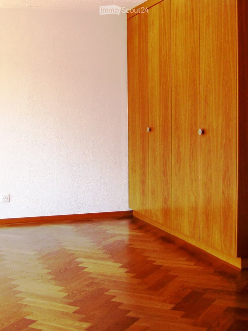 Empty room with wooden flooring and light-colored walls, featuring built-in wooden cabinets on one side.