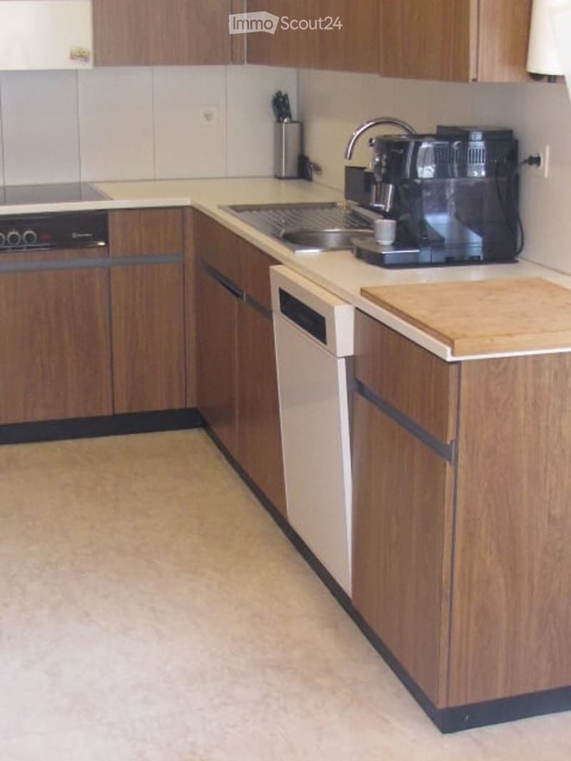 A modern kitchen with wooden cabinets, a white countertop, a sink, a coffee maker, and a dishwasher.