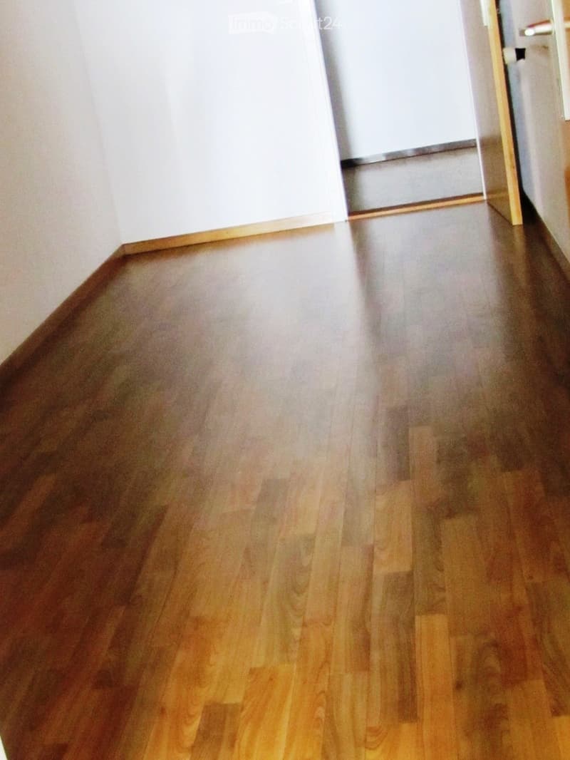 Empty room with polished wooden flooring and white walls, featuring a doorway leading to another space.