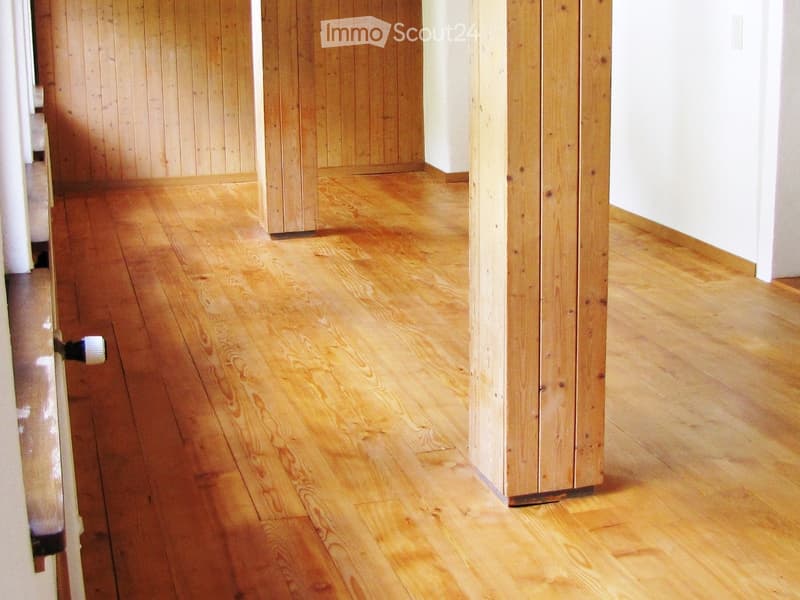 Empty hallway with polished wooden flooring and light-colored walls, featuring a wooden pillar and a partially visible door.