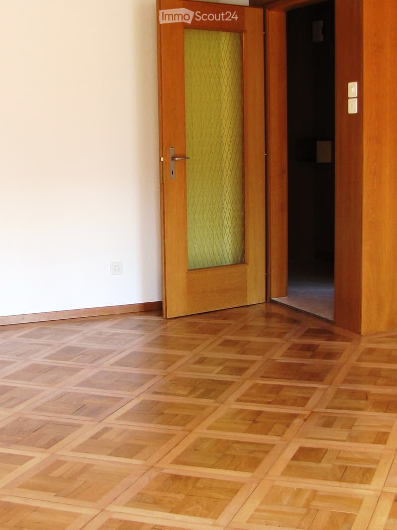 A narrow hallway with wooden panel walls and a frosted glass window with a wooden frame. The walls are light-colored with a geometric pattern, and the floor is not visible.