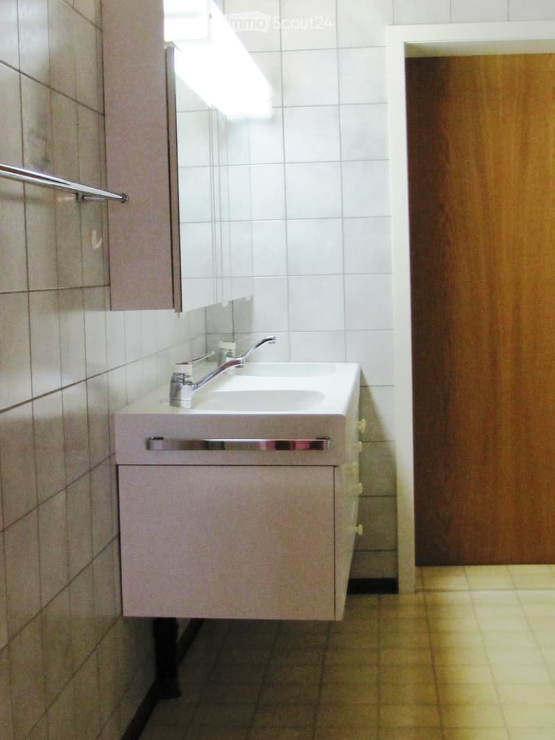 Bathroom with white tiled walls, a shower area, a faucet, and a cabinet.