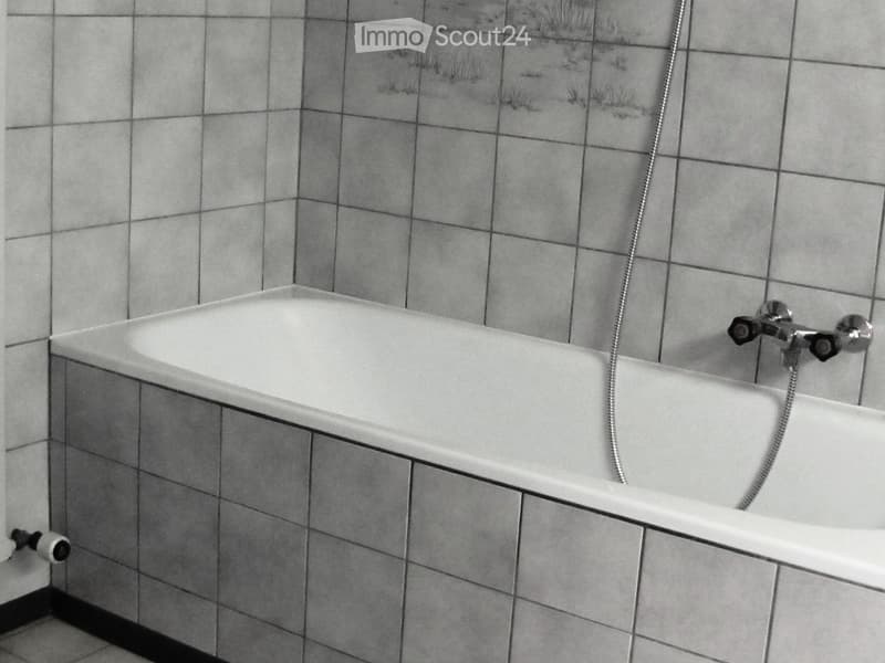 Bathroom with a white bathtub, tiled walls, and a faucet with a flexible hose.